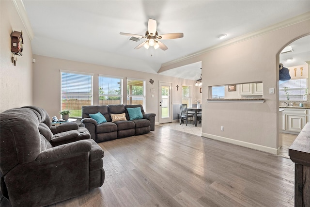 living room with light wood finished floors, ornamental molding, arched walkways, baseboards, and ceiling fan