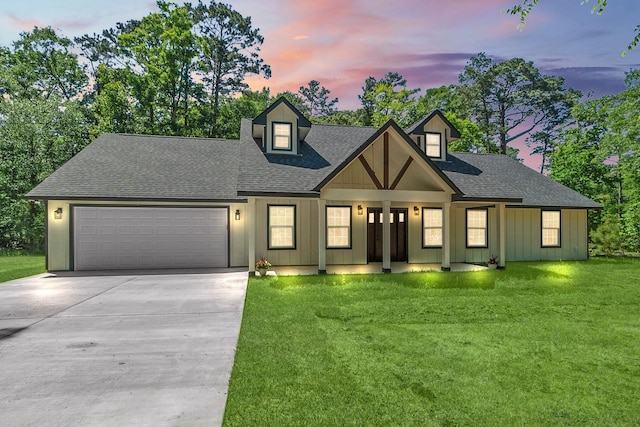 view of front of property with a front lawn, driveway, an attached garage, a shingled roof, and board and batten siding
