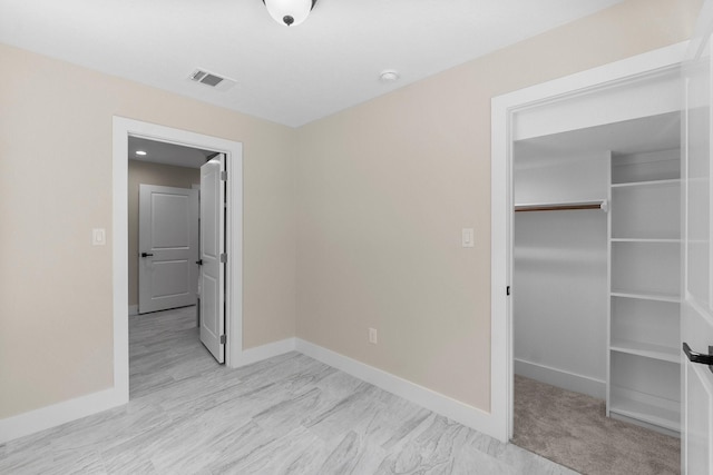 unfurnished bedroom featuring a walk in closet, baseboards, visible vents, and a closet