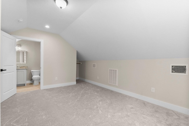 additional living space with baseboards, vaulted ceiling, visible vents, and light carpet