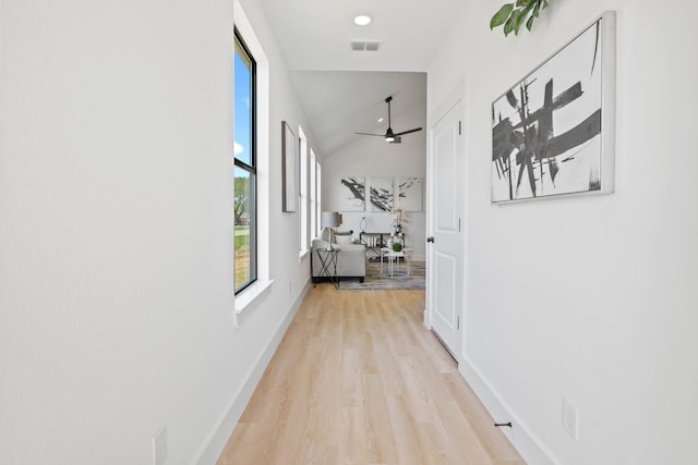 hallway featuring baseboards, visible vents, high vaulted ceiling, and light wood-style floors