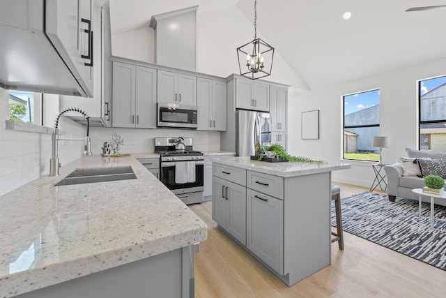 kitchen featuring a breakfast bar, a sink, light wood-style floors, gray cabinetry, and appliances with stainless steel finishes