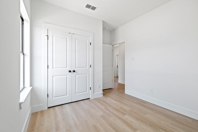 unfurnished bedroom featuring baseboards, a closet, visible vents, and light wood-style flooring