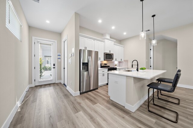 kitchen featuring a sink, light wood-style flooring, a kitchen bar, white cabinets, and appliances with stainless steel finishes