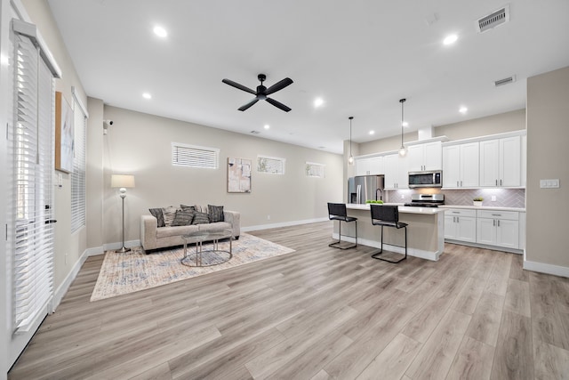 living room with light wood-style floors, ceiling fan, baseboards, visible vents, and recessed lighting
