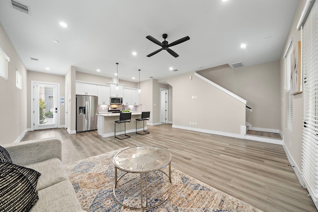 living room with baseboards, a ceiling fan, light wood finished floors, and visible vents