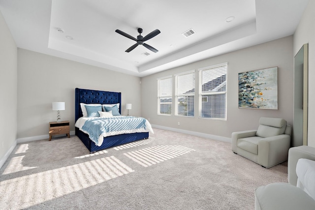 bedroom featuring a tray ceiling, visible vents, baseboards, carpet, and a ceiling fan