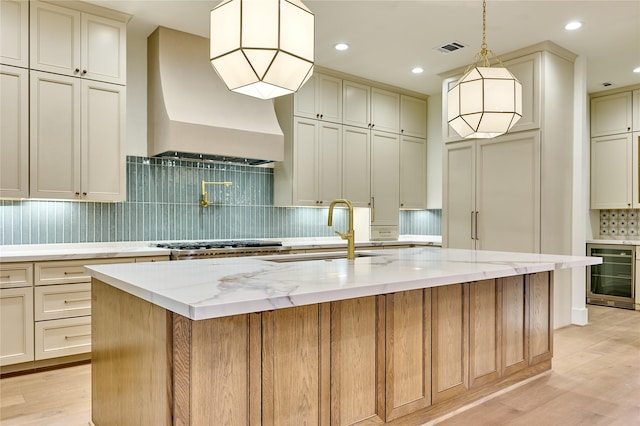 kitchen featuring beverage cooler, custom range hood, light wood finished floors, a sink, and visible vents