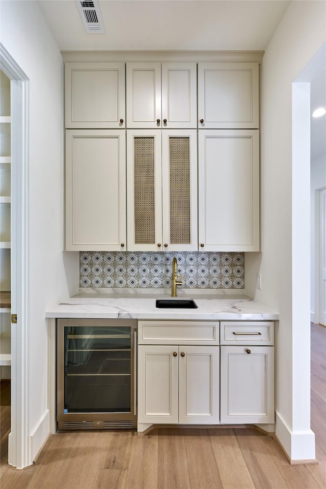 bar featuring a sink, decorative backsplash, light wood-type flooring, visible vents, and beverage cooler