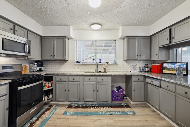 1858 Wood Orchard Dr, Missouri City, TX 77489 - kitchen featuring decorative backsplash, stainless steel appliances, a sink, gray cabinetry, and a textured ceiling