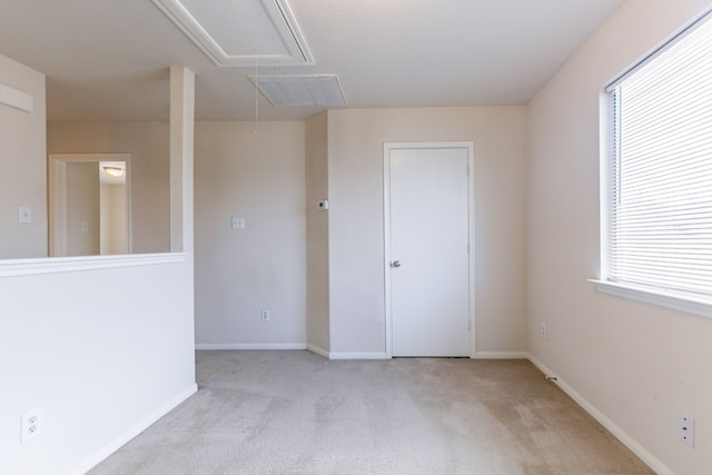 carpeted empty room with attic access, visible vents, and baseboards