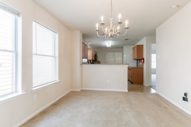 interior space with brown cabinets, light carpet, a chandelier, and baseboards