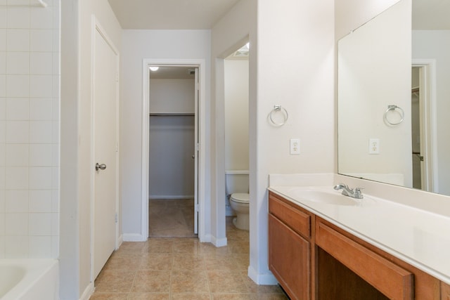 bathroom with a spacious closet, a washtub, toilet, and vanity