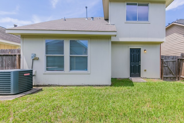 rear view of property featuring fence, a lawn, a shingled roof, and central AC unit