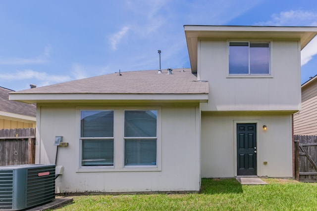 rear view of property featuring cooling unit, a lawn, a shingled roof, and fence