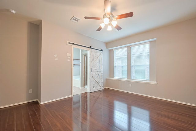 unfurnished bedroom with a barn door, baseboards, visible vents, wood finished floors, and ceiling fan