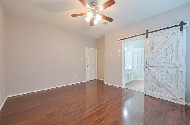 empty room featuring a barn door, baseboards, visible vents, a ceiling fan, and wood finished floors