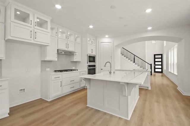 122 Canary Island Cir, Montgomery, TX 77316 - kitchen featuring under cabinet range hood, arched walkways, a sink, stainless steel microwave, and light wood-type flooring