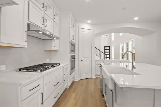 122 Canary Island Cir, Montgomery, TX 77316 - kitchen featuring stainless steel appliances, under cabinet range hood, a sink, arched walkways, and light wood-style flooring