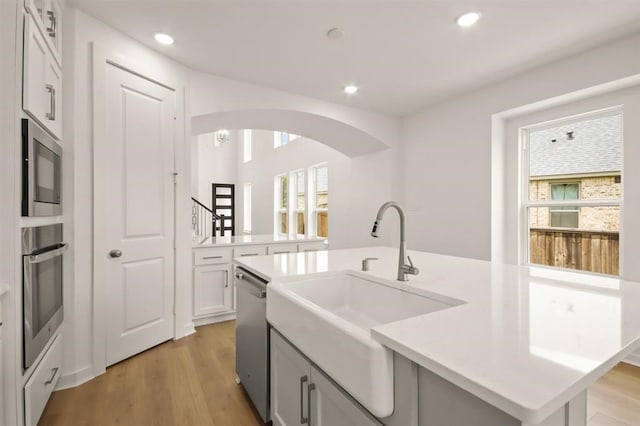 122 Canary Island Cir, Montgomery, TX 77316 - kitchen featuring appliances with stainless steel finishes, a sink, a center island with sink, arched walkways, and light wood-style flooring
