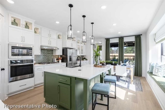122 Canary Island Cir, Montgomery, TX 77316 - kitchen featuring appliances with stainless steel finishes, light wood-style flooring, light countertops, decorative backsplash, and green cabinetry