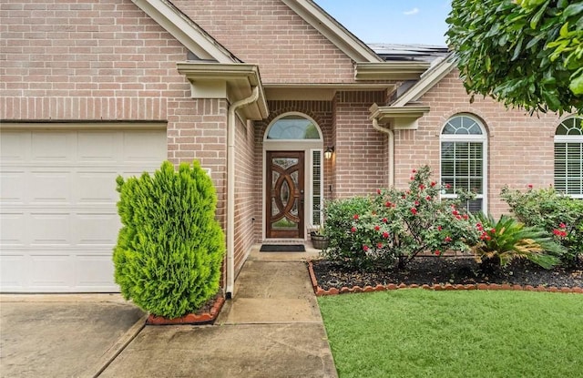 entrance to property featuring a garage, brick siding, and a lawn