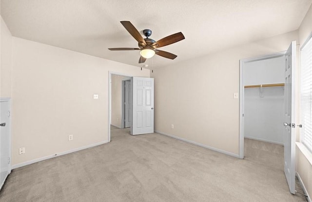 unfurnished bedroom with a ceiling fan, a walk in closet, a closet, baseboards, and light colored carpet