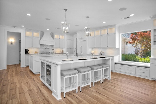 16059 Walden Rd, Conroe, TX 77356 - kitchen with an inviting chandelier, a kitchen island with sink, visible vents, backsplash, and custom range hood