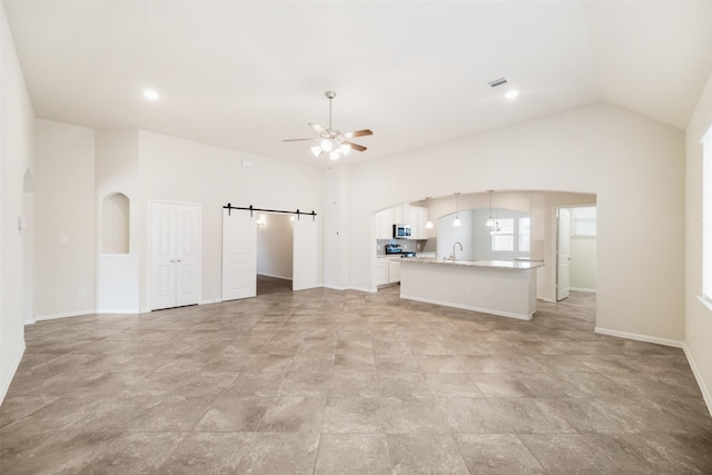 unfurnished living room with a barn door, a ceiling fan, a sink, arched walkways, and visible vents