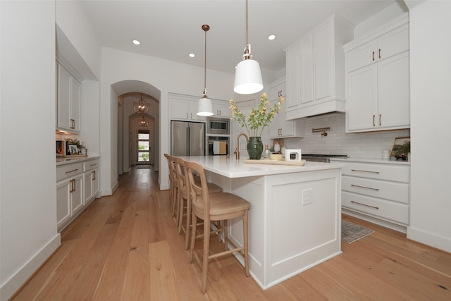 14924 Scarlet Branch Dr, Conroe, TX 77302 - kitchen featuring arched walkways, backsplash, light wood-style floors, light countertops, and appliances with stainless steel finishes