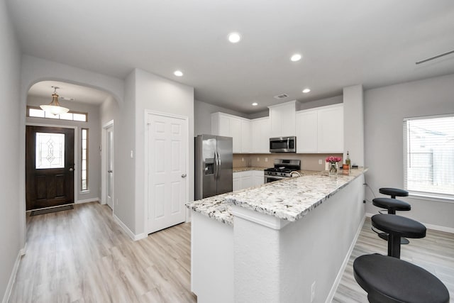 kitchen with white cabinets, stainless steel appliances, arched walkways, light wood-type flooring, and a peninsula