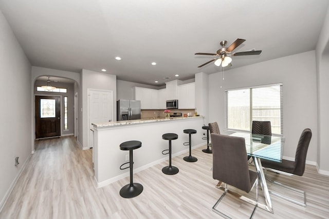 dining room featuring recessed lighting, light wood finished floors, a ceiling fan, arched walkways, and baseboards