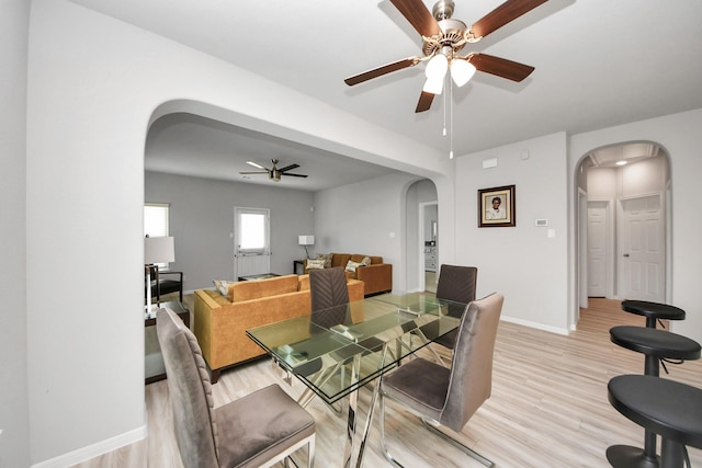 dining space with light wood-type flooring, baseboards, arched walkways, and ceiling fan