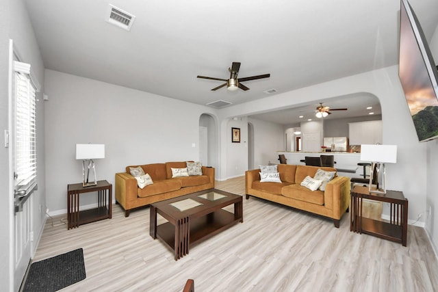 living room featuring arched walkways, light wood-type flooring, visible vents, and a ceiling fan