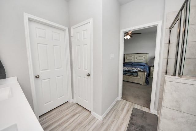 bathroom with a tile shower, ensuite bathroom, baseboards, wood finished floors, and vanity