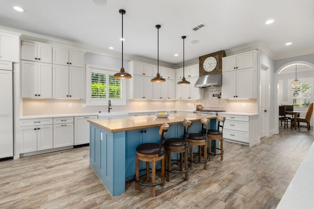 kitchen featuring light countertops, wall chimney range hood, light wood finished floors, and a sink
