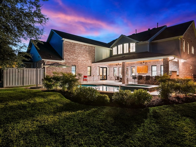 rear view of house with an in ground hot tub, brick siding, a lawn, a patio, and an outdoor pool