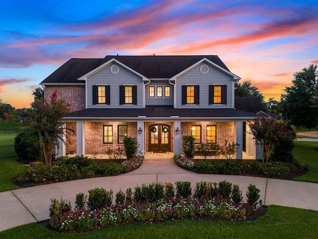 traditional home with covered porch, a front yard, french doors, and brick siding