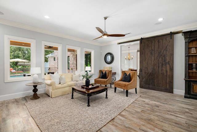 living room featuring a barn door, crown molding, ceiling fan with notable chandelier, and plenty of natural light