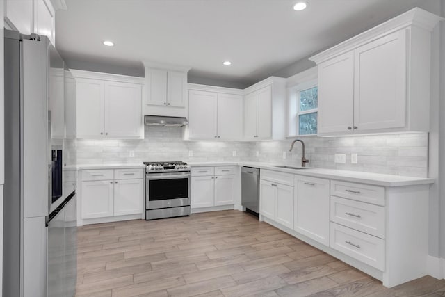 kitchen with under cabinet range hood, stainless steel appliances, light countertops, a sink, and white cabinetry