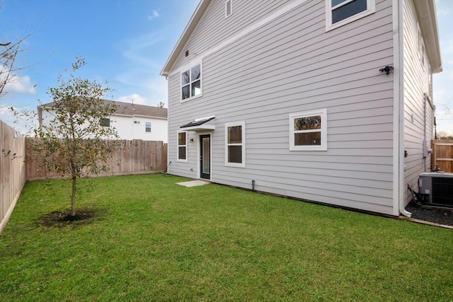 back of property with a fenced backyard, cooling unit, and a lawn