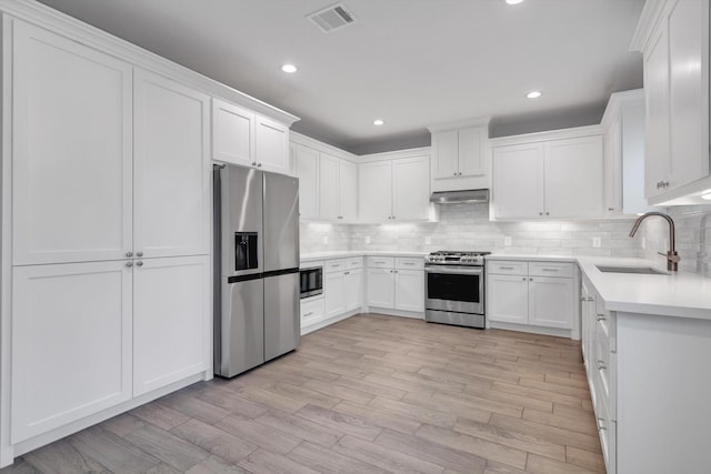 kitchen with under cabinet range hood, backsplash, visible vents, a sink, and appliances with stainless steel finishes