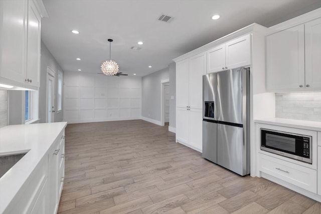 kitchen featuring built in microwave, light countertops, stainless steel refrigerator with ice dispenser, white cabinetry, and visible vents