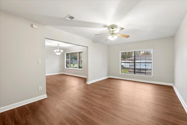 spare room featuring ceiling fan with notable chandelier, visible vents, dark wood-type flooring, and a healthy amount of sunlight
