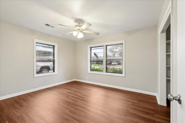 spare room featuring wood finished floors, visible vents, a ceiling fan, and baseboards