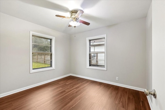 spare room featuring baseboards, dark wood-type flooring, ceiling fan, and a healthy amount of sunlight