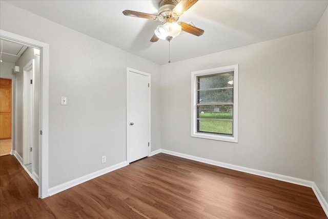 unfurnished bedroom with attic access, baseboards, a ceiling fan, and wood finished floors