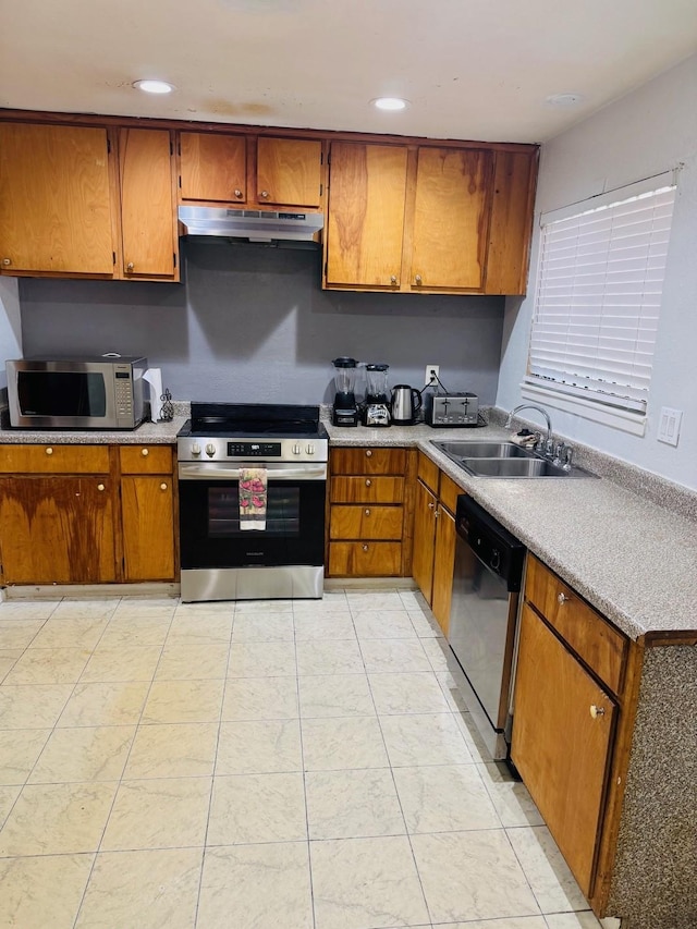 kitchen featuring a sink, brown cabinetry, appliances with stainless steel finishes, light countertops, and under cabinet range hood