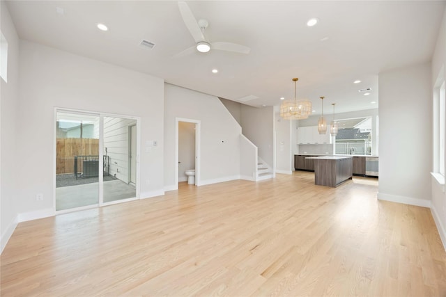 unfurnished living room featuring stairway, ceiling fan with notable chandelier, light wood finished floors, visible vents, and recessed lighting