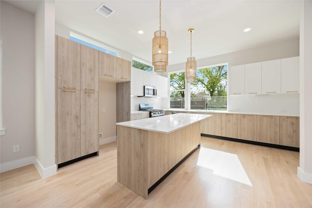kitchen featuring modern cabinets, light brown cabinets, appliances with stainless steel finishes, and light wood-style flooring